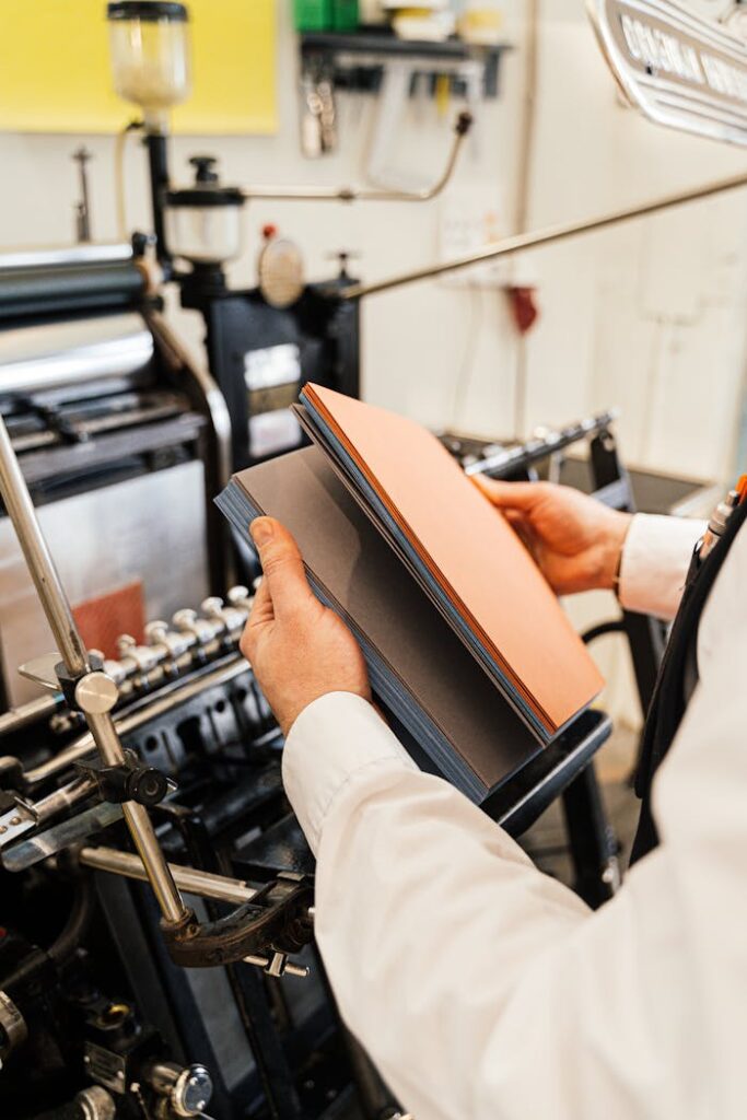 Person holding papers near a printing press in a workshop setting.